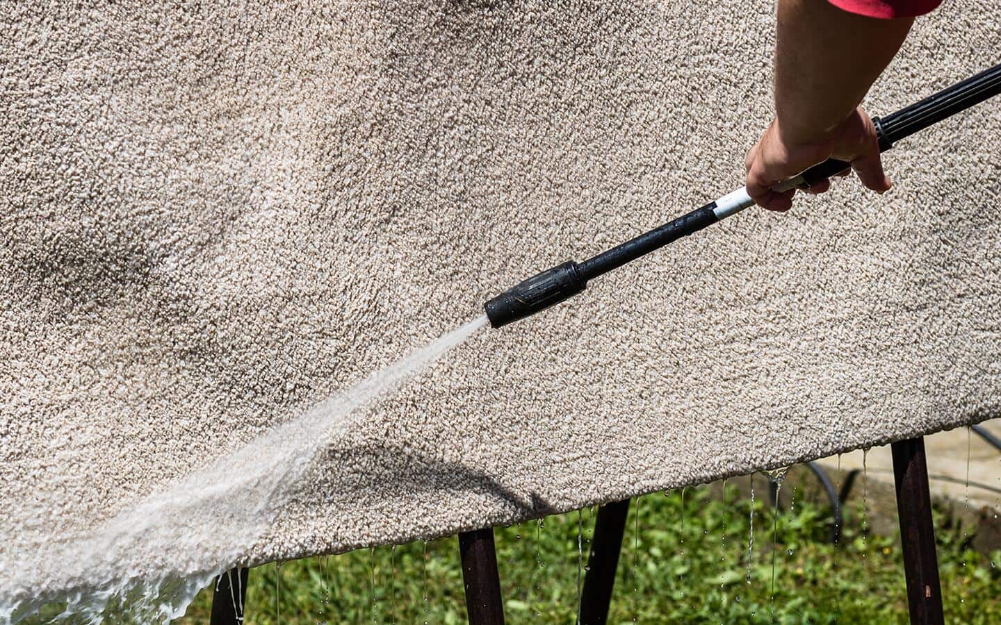 A person rinsing an outdoor rug with water.