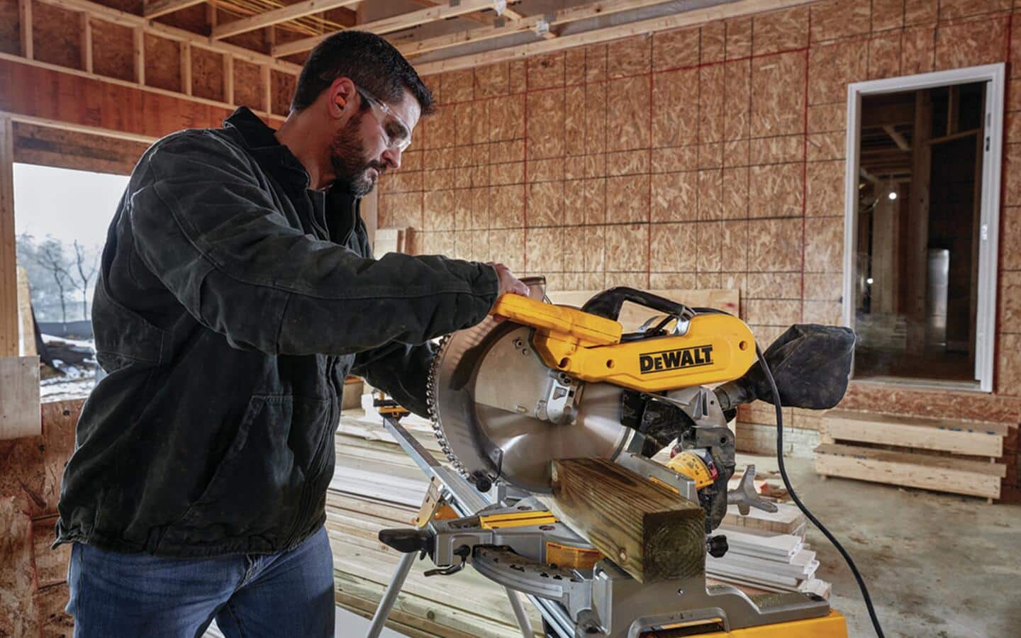 Someone in safety glasses using a yellow miter saw to cut an angle on lumber.