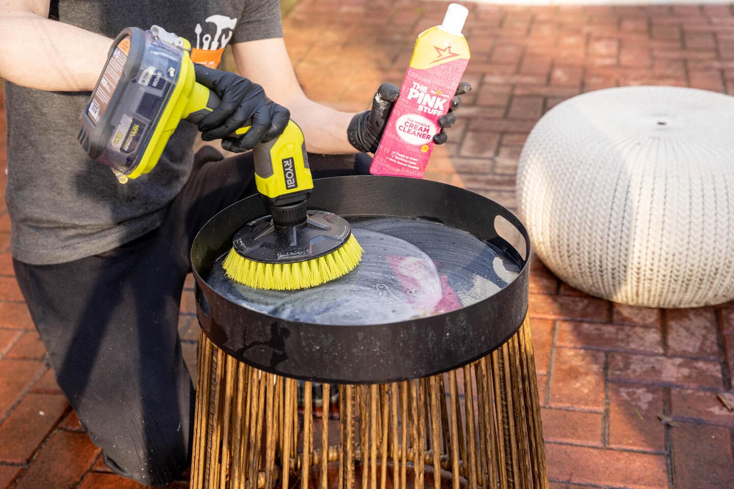 Tyson uses the brush attachment on his hand-held scrubber to clean a smaller black tray on one of his patio furniture's side tables. 
