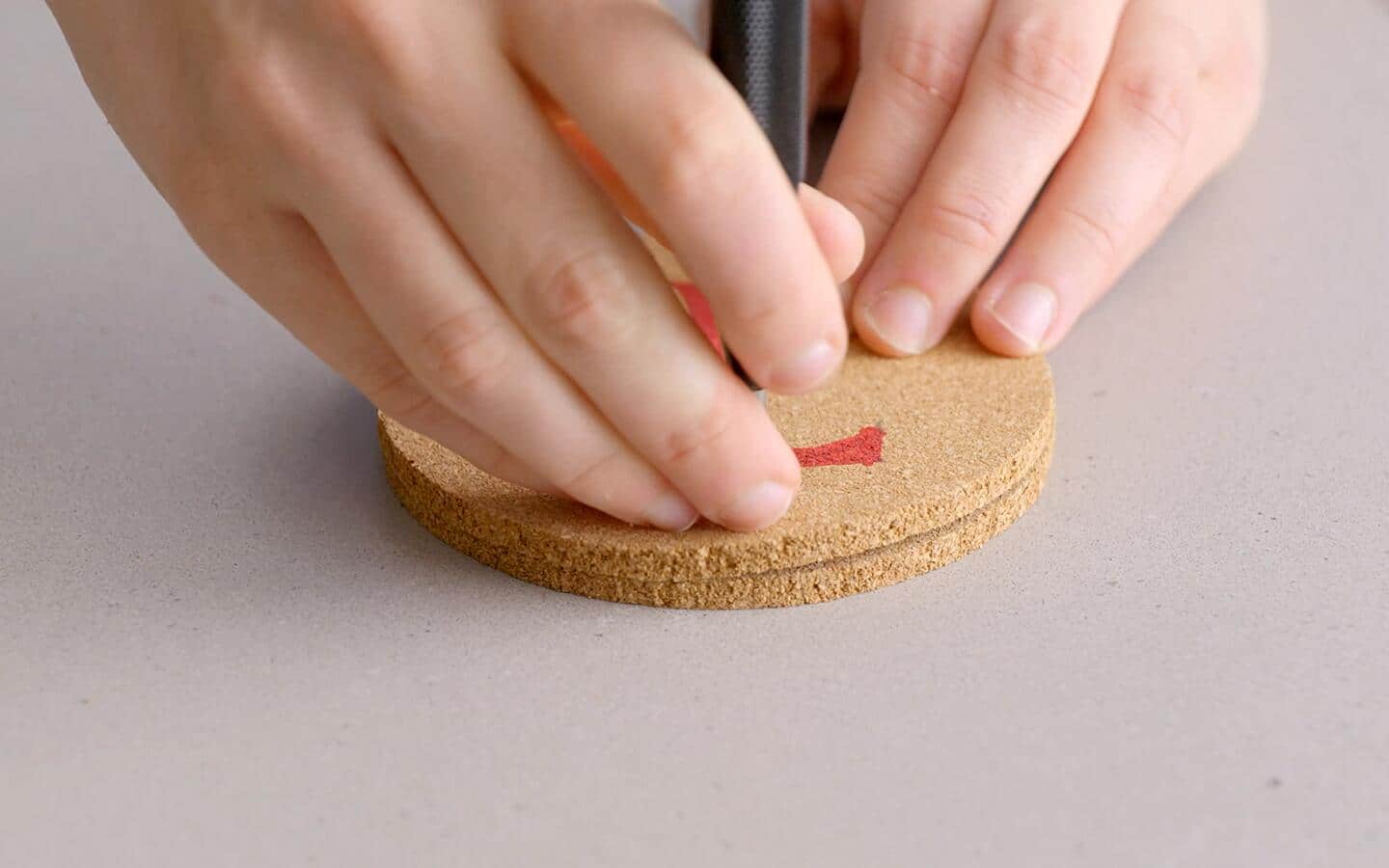 A single hole punch is used to make a hole in a cork coaster.