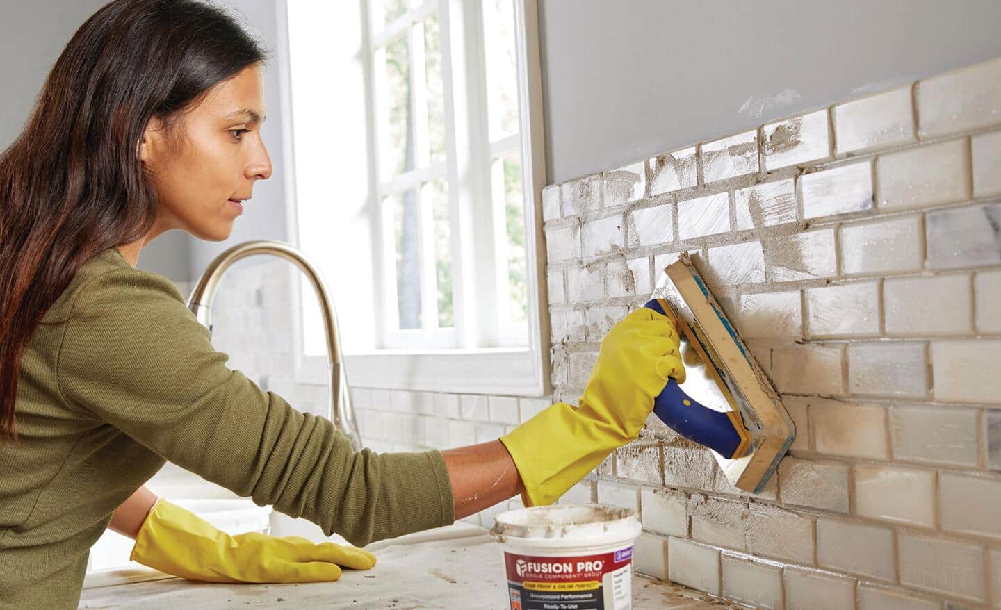 A person applies grout to tile.