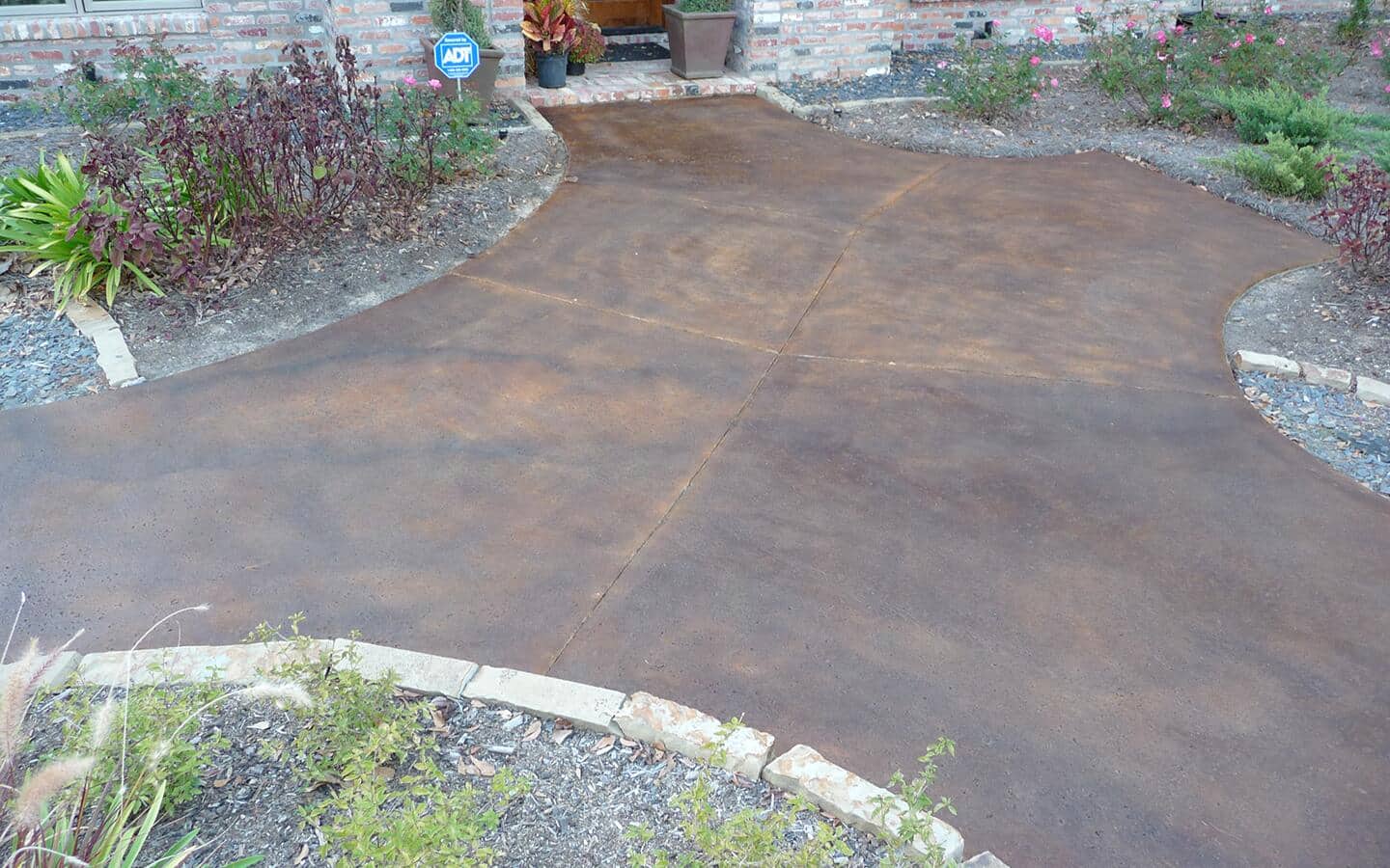 A concrete patio stained with brown stain bordered by gardens.