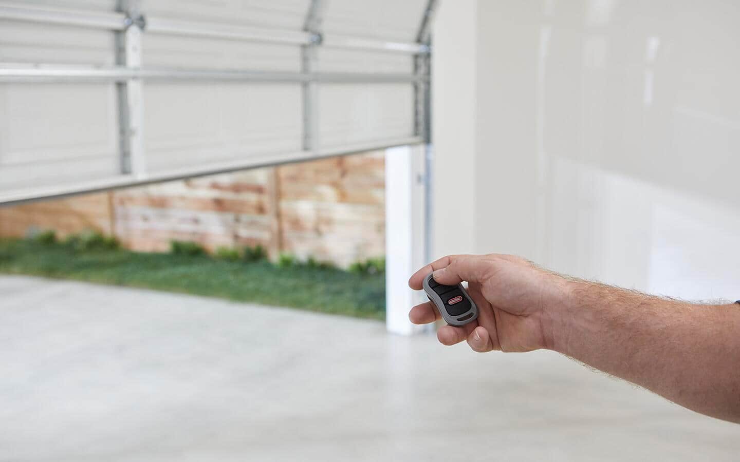 Person uses a remote control to test the smart garage door opener in front of a garage door