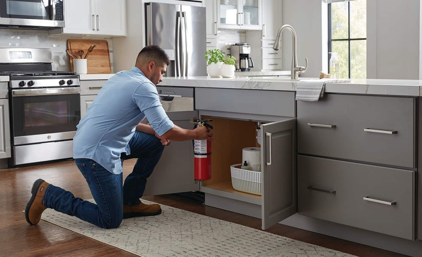 Man putting a fire extinguisher under a kitchen cabinet.