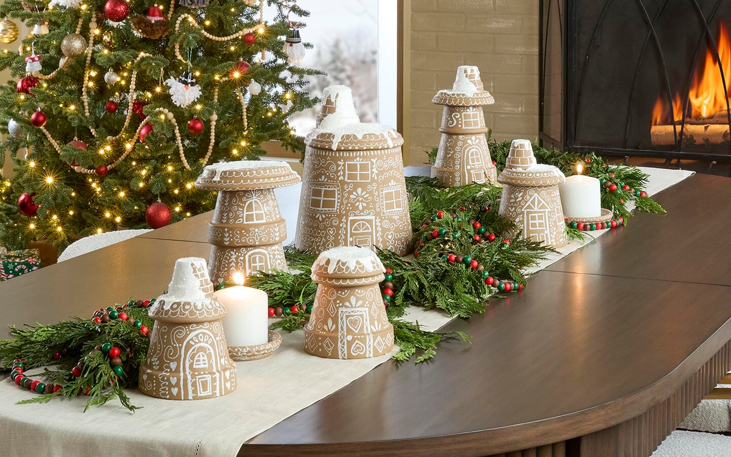 A gingerbread village set up on a table in front of a holiday tree.