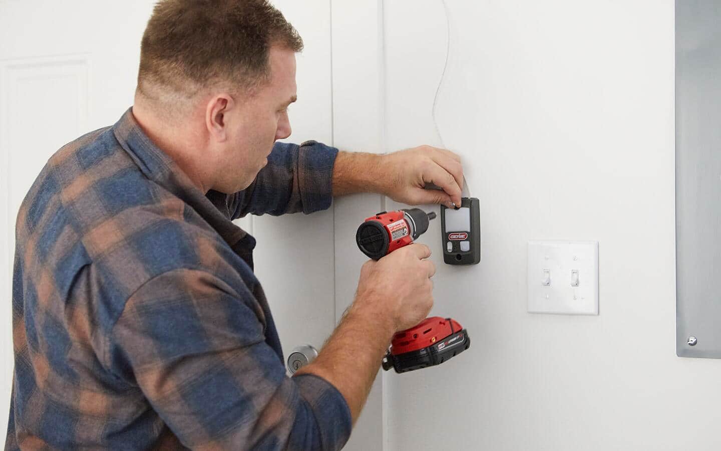 Person uses a cordless drill to install a smart garage door keypad to a wall