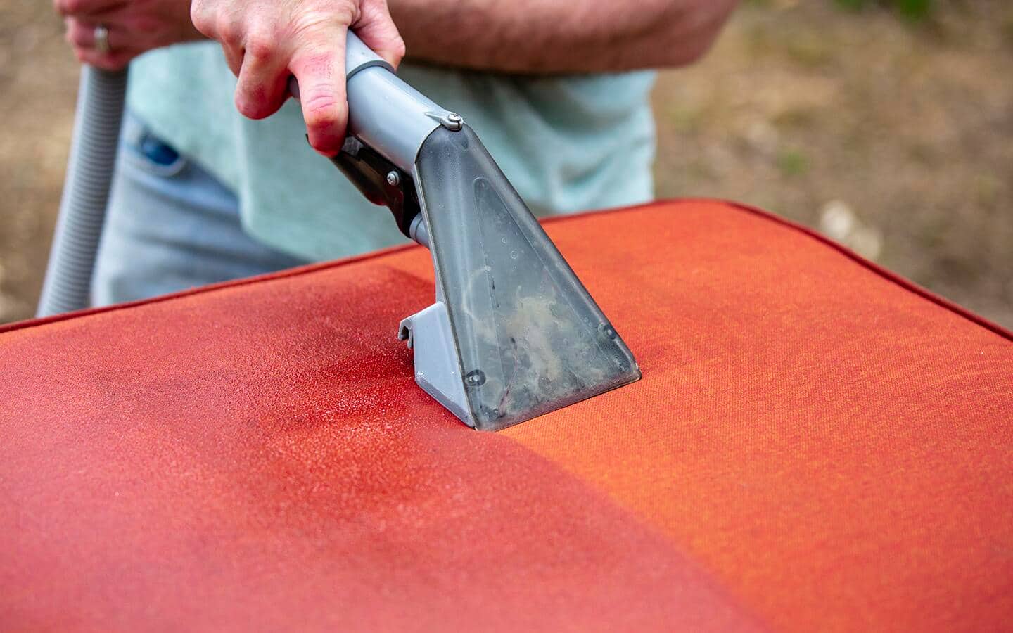A person using a spot detailer to clean patio chair fabric