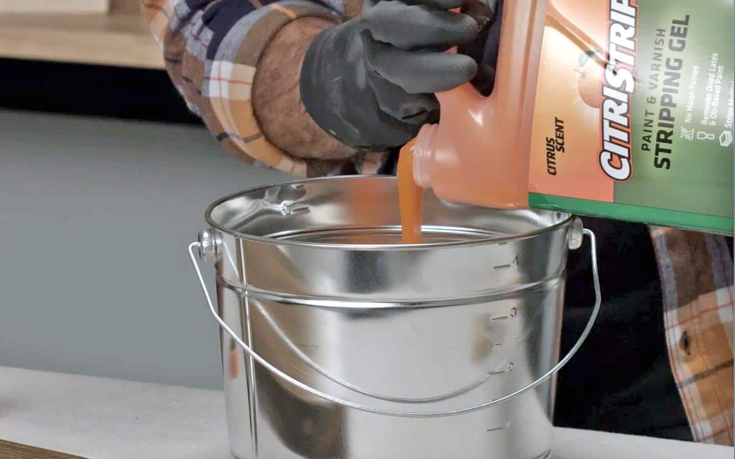 A person pours paint stripper into a bucket.