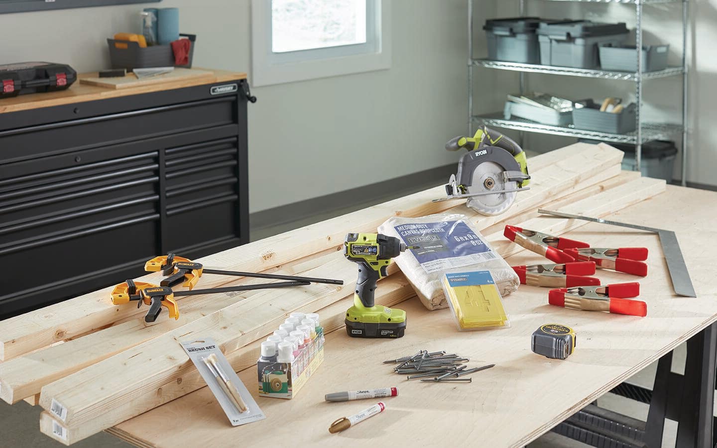 Lumber, a drill, a circular saw, clamps and other tools and materials lay on a work bench. Lumber, a drill, a circular saw, clamps and other tools and materials lay on a work bench.