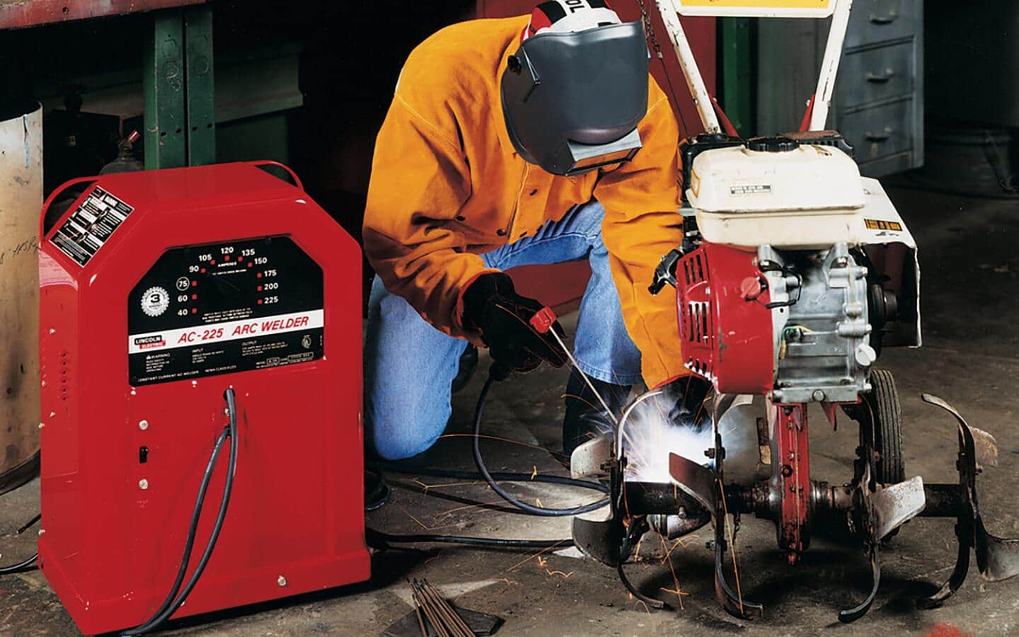 A helmeted person in a gold jacket kneels down while welding.