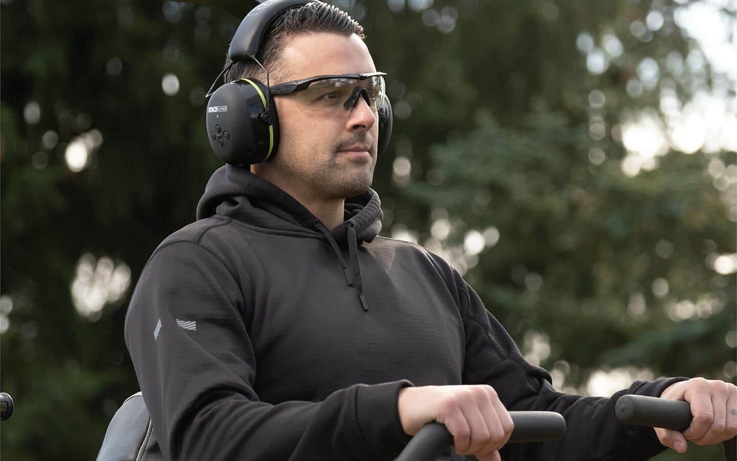 A man wears safety glasses and hearing protection while operating a lawn mower. A man wears safety glasses and hearing protection while operating a lawn mower.