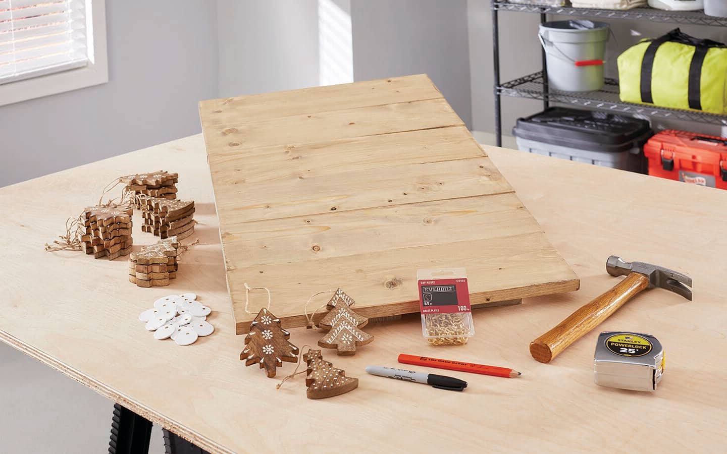 A finished wood Christmas craft board, hammer and wood tree hangers placed on a table.