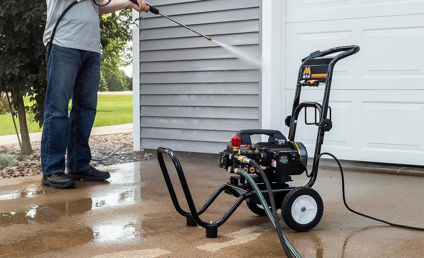 A man using an electric pressure washer to clean a garage door.