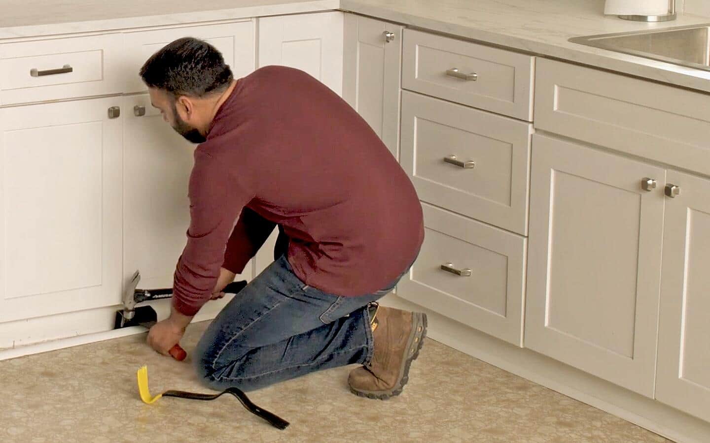 A person removing a baseboard with a hammer and prybar. A person removing a baseboard with a hammer and prybar.