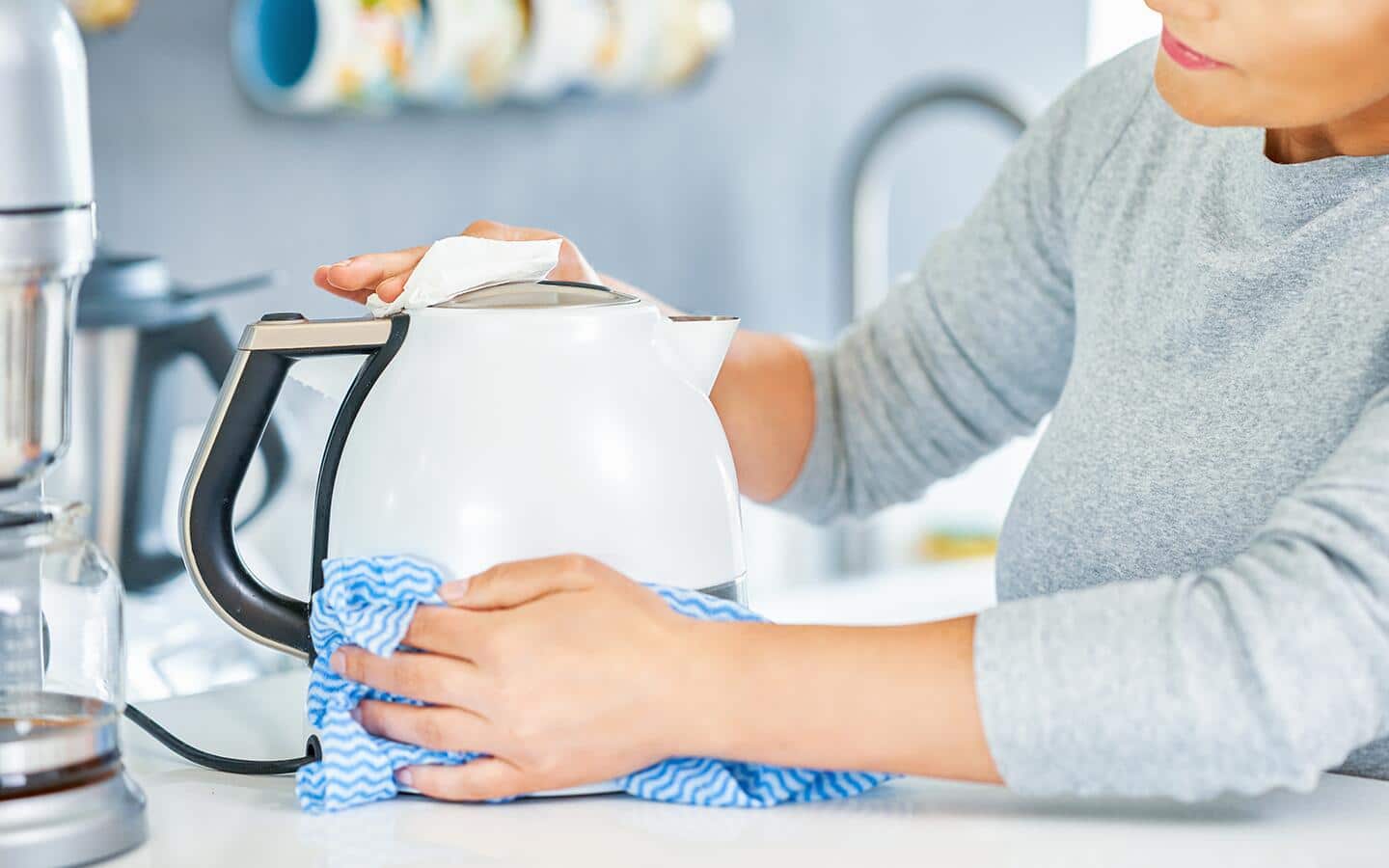 A person cleans an electric kettle with a cloth.