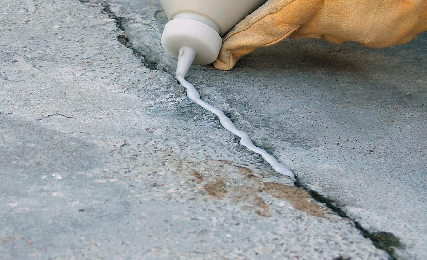 A person using a tube of filler to repair a small crack in a concrete driveway.