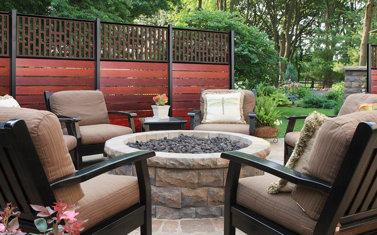 A patio with chairs, a wall and a stone fire pit.