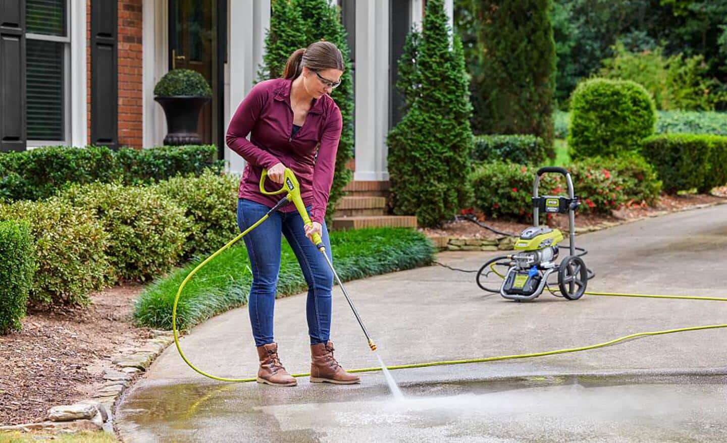A woman pressure washes her driveway. 