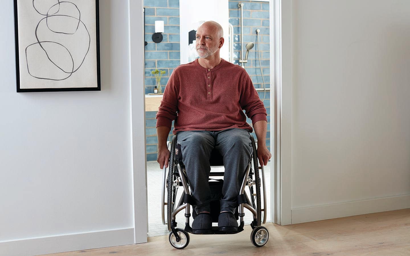 A man in a wheelchair exiting the doorway of a bathroom. A man in a wheelchair exiting the doorway of a bathroom.