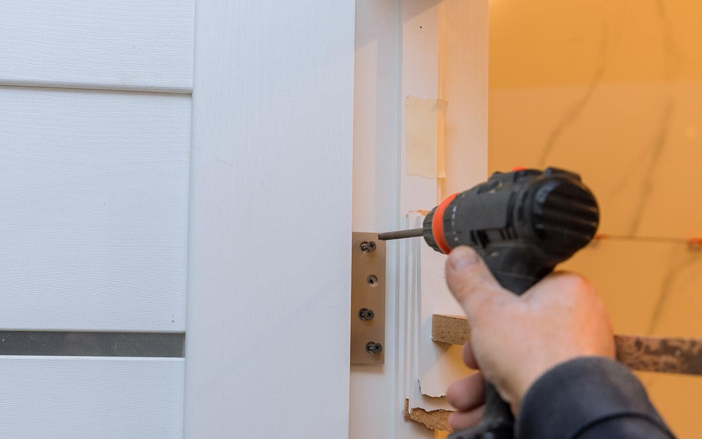 A person installing a screw into a bifold door plate with a cordless drill. A person installing a screw into a bifold door plate with a cordless drill.
