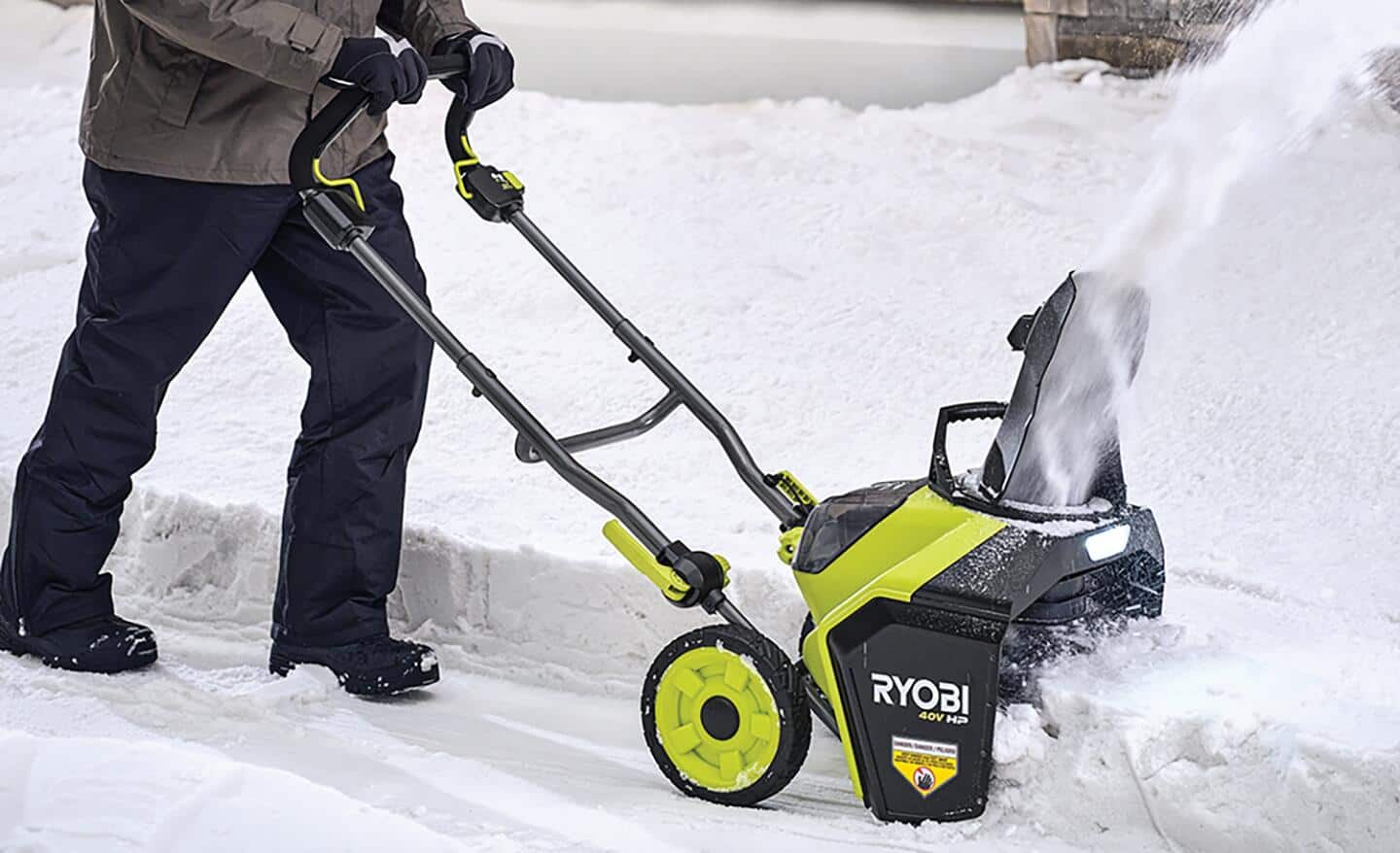 A person using a green single-stage snow blower to clear a snowdrift.