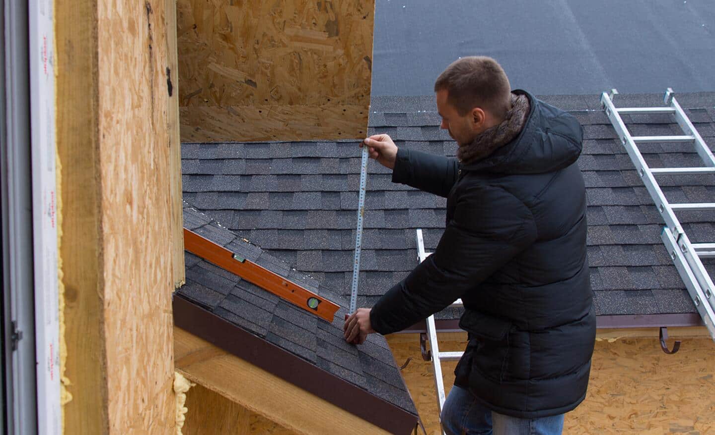 A person wearing a winter coat while measuring a roof.