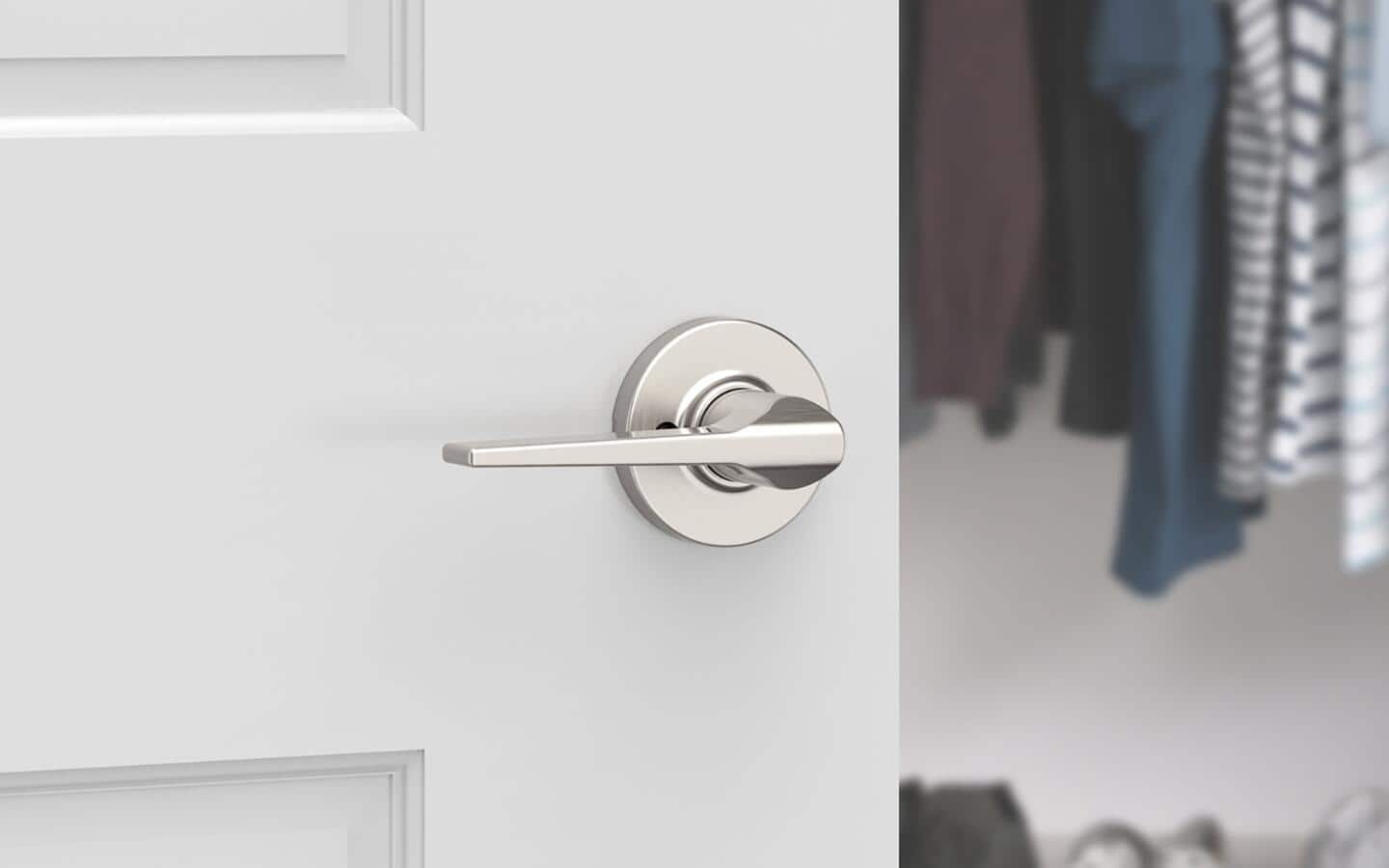 A white closet door with a silver handle stands open to show clothes inside. A white closet door with a silver handle stands open to show clothes inside.
