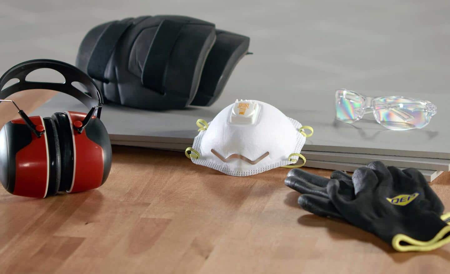 Gloves, kneepads, safety glasses and other safety equipment lying on tile.