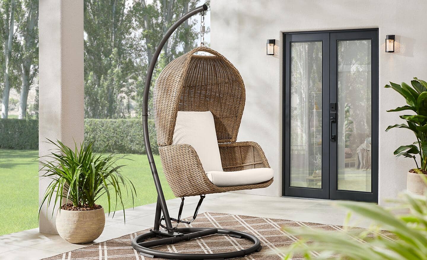 An egg-shaped wicker swing with off-white cushions on a patio.