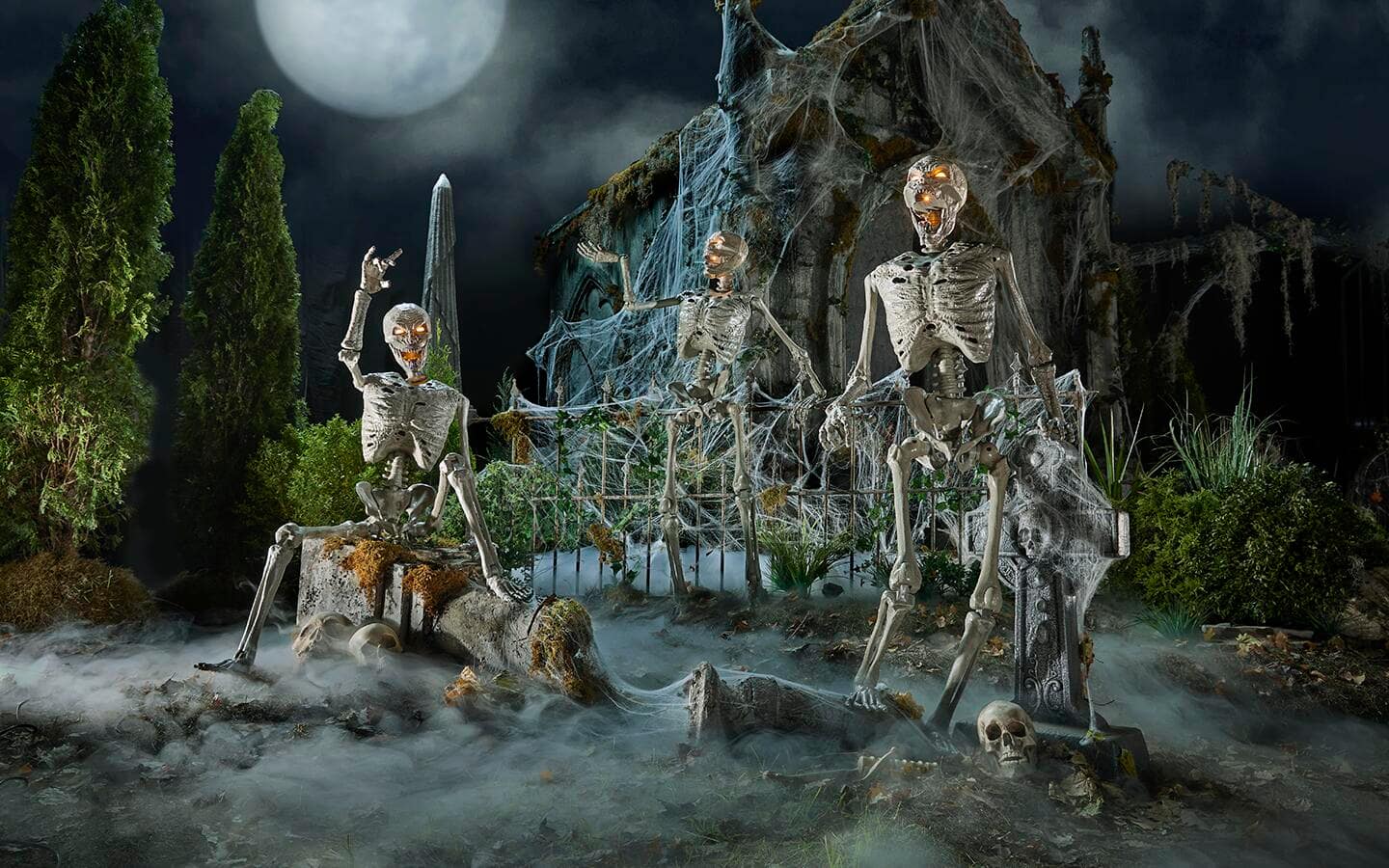 Skeletal creatures hanging out in a graveyard decorated with fog and wispy webs. 