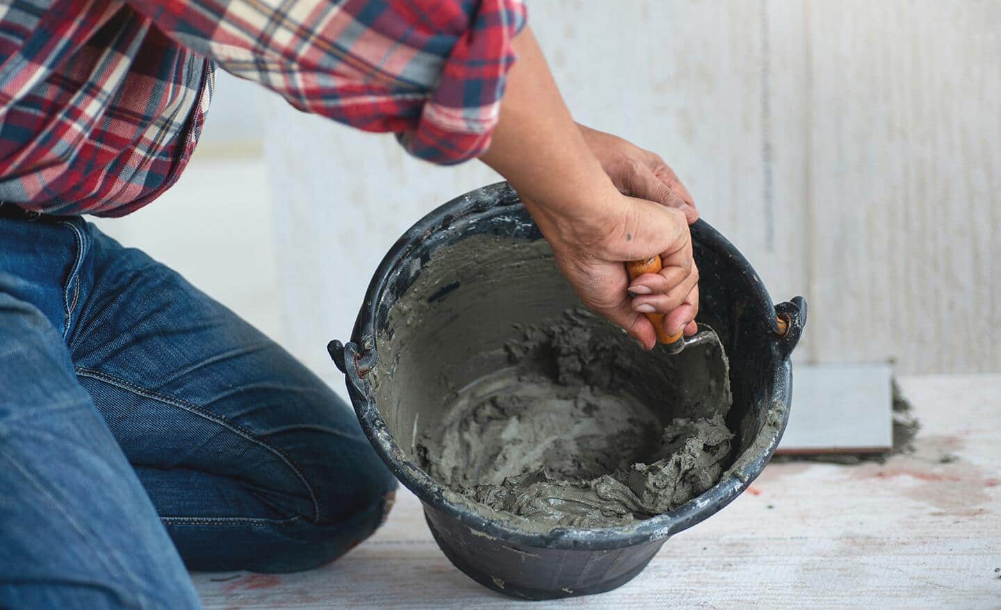 A man stirring cement in a bucket with a trowel.