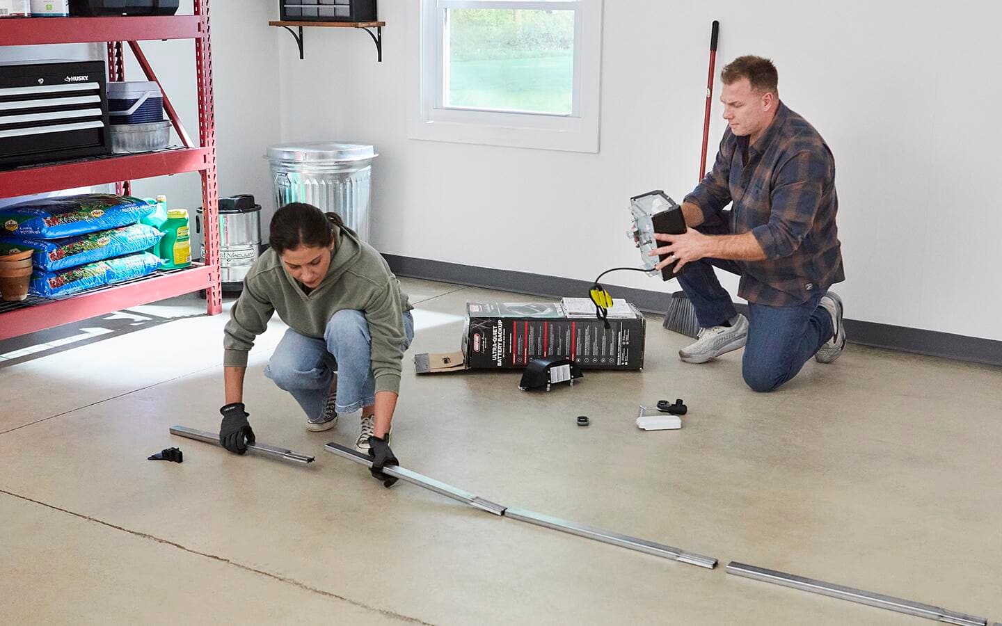 Two people assemble the carriage tube for a smart garage door opener on the floor of a garage