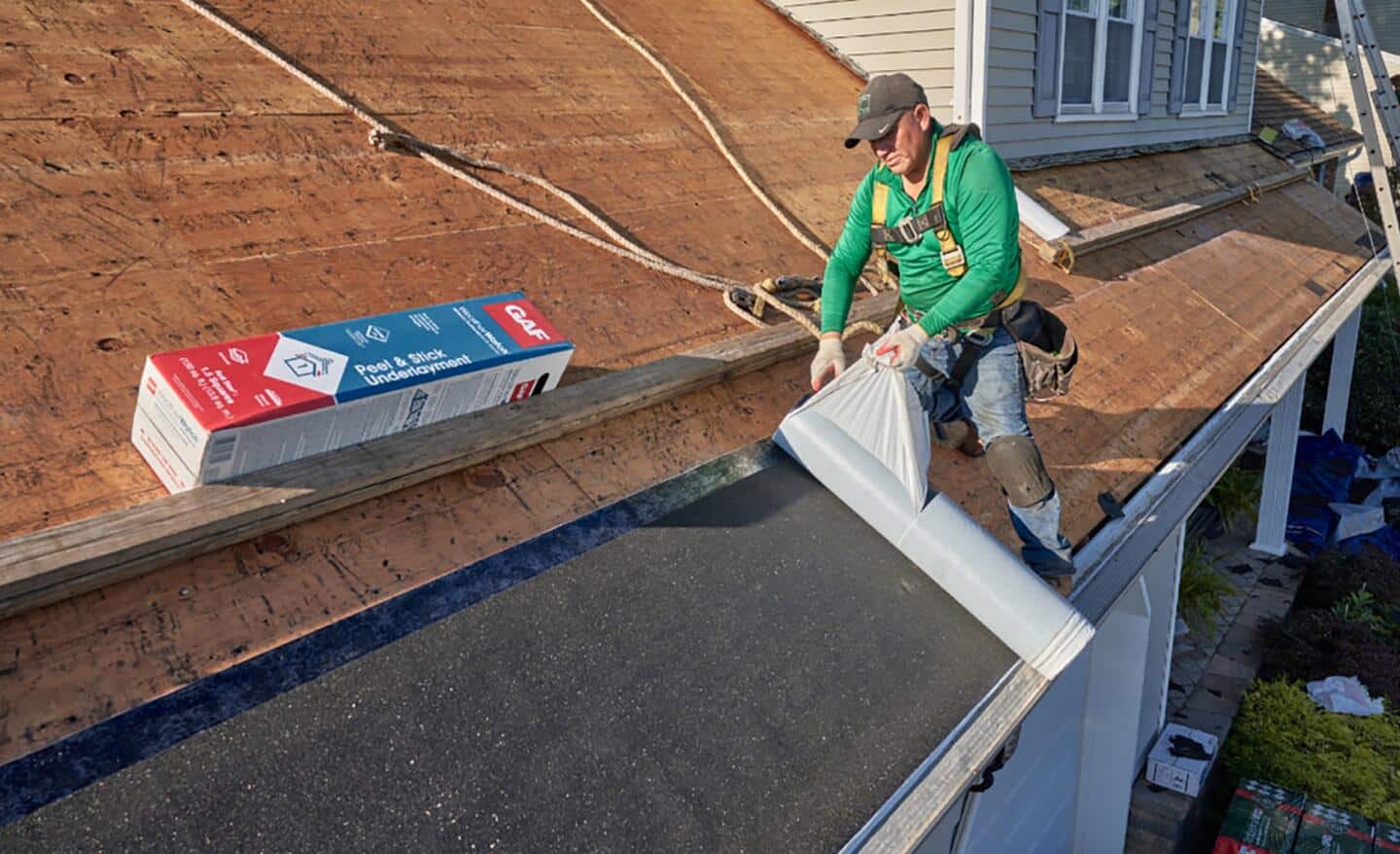 A worker rolls out membrane roofing material on a rooftop.