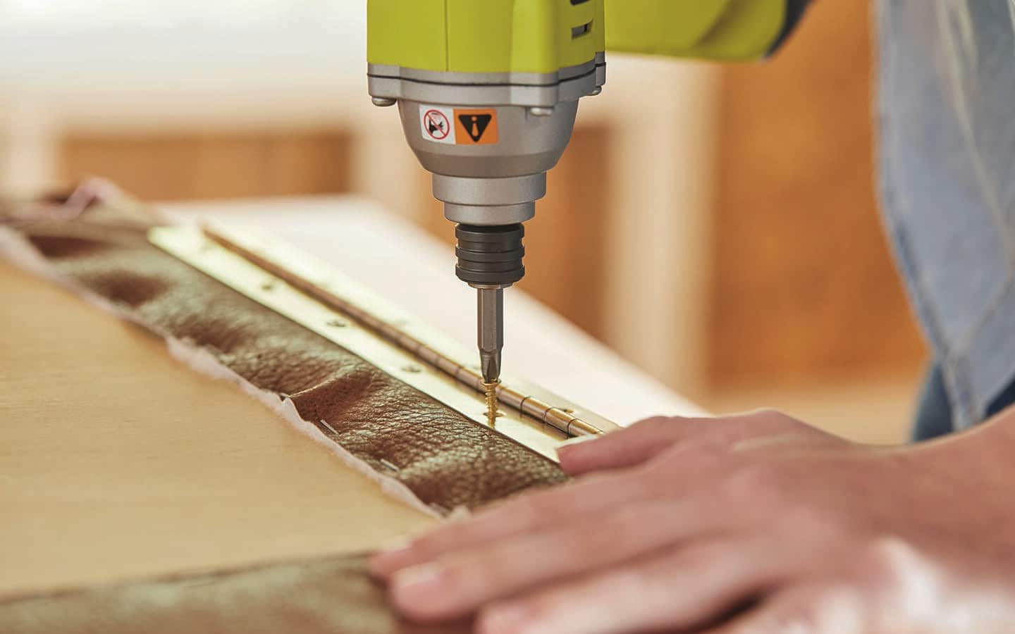 A person uses a power drill to attach a piano hinge. A person uses a power drill to attach a piano hinge.