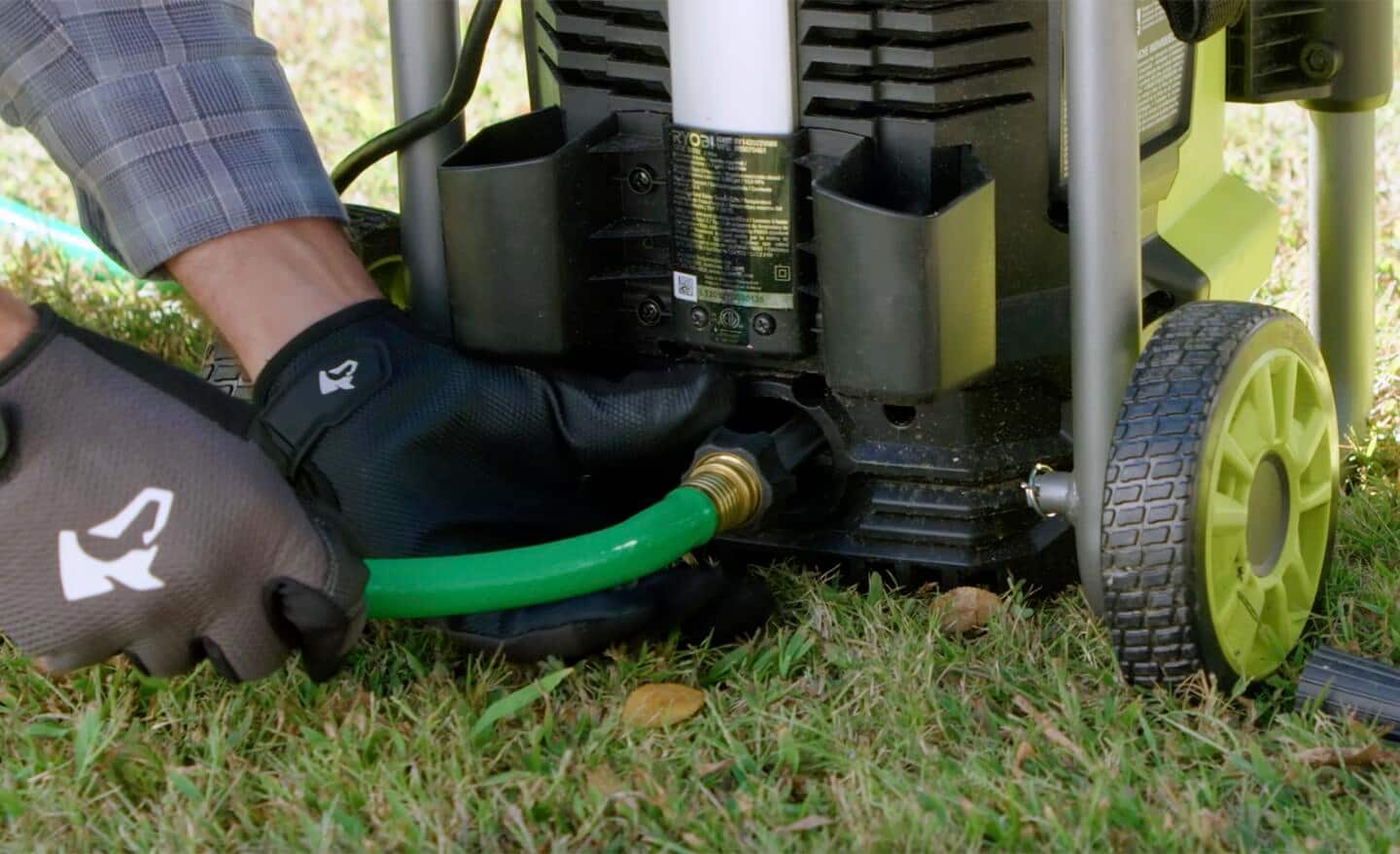 A person attaches a garden hose to the water inlet on their pressure washer. 