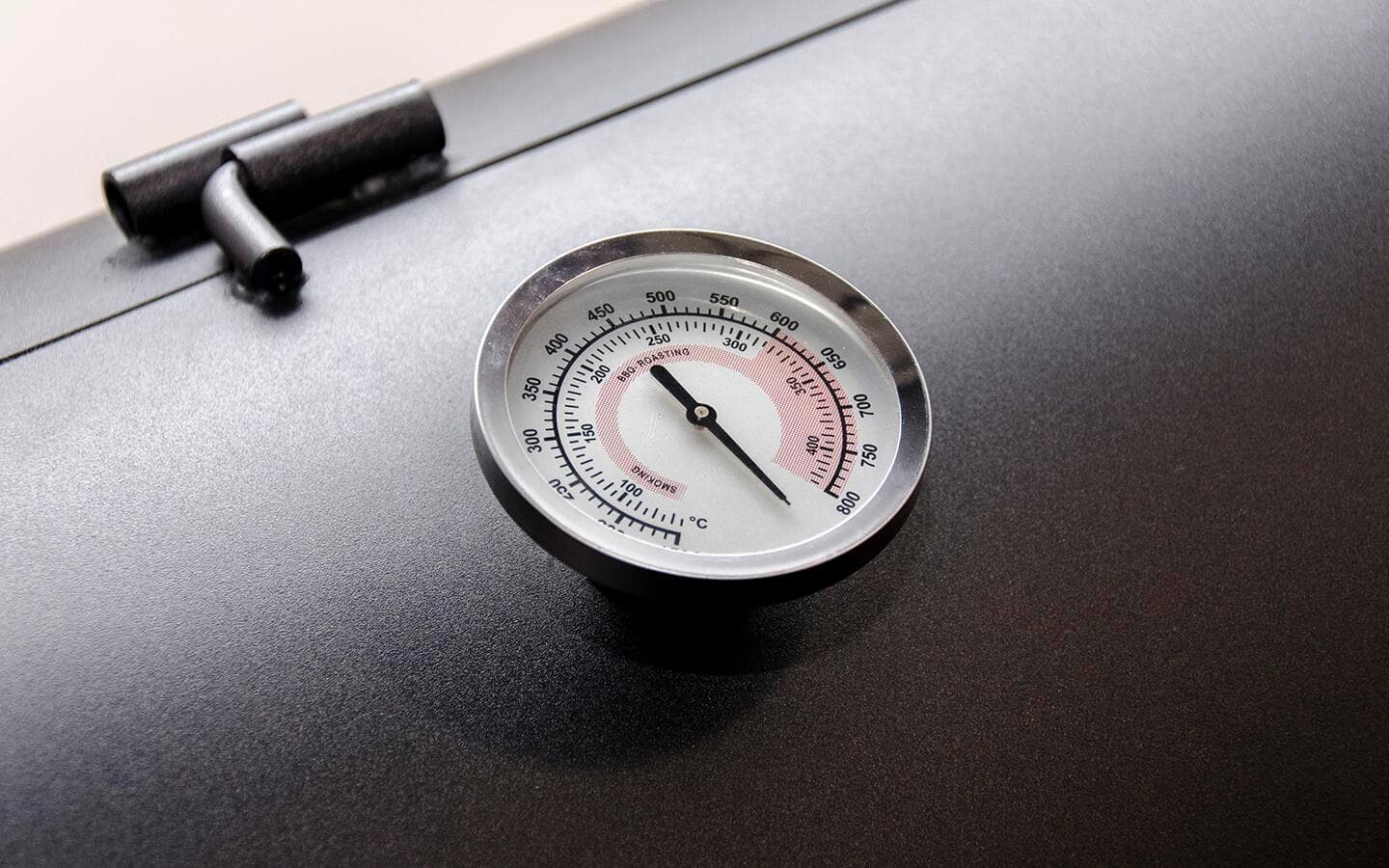 A thermometer with a white display on a black smoker.