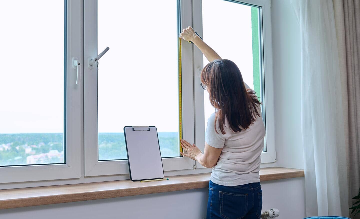 A person measures a window's height using a tape measure.