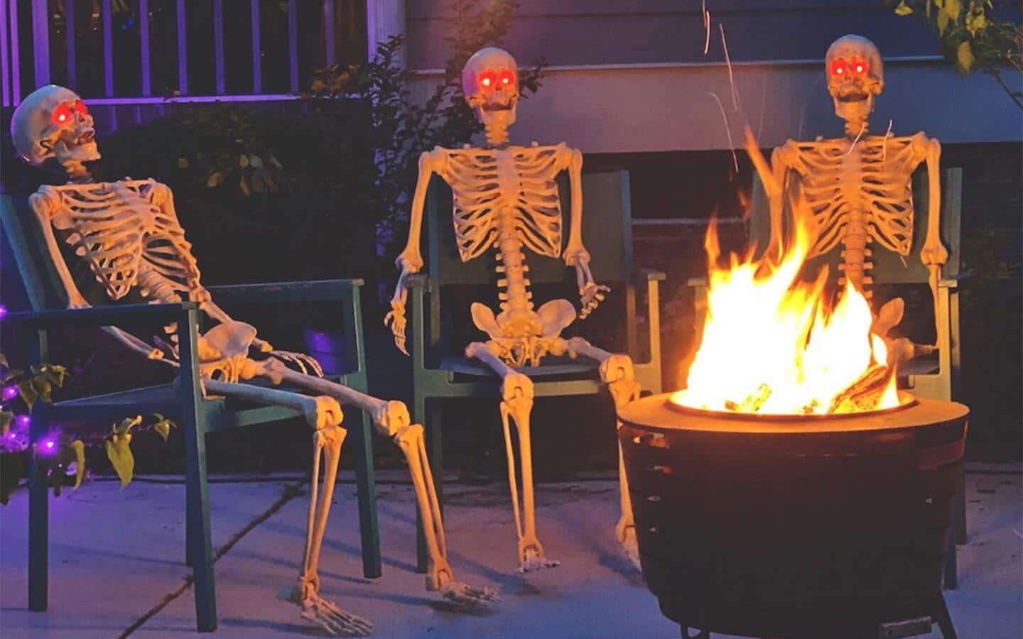 A DIY Halloween scene of a group of skeletons seated around a fire pit outside a home. A DIY Halloween scene of a group of skeletons seated around a fire pit outside a home.