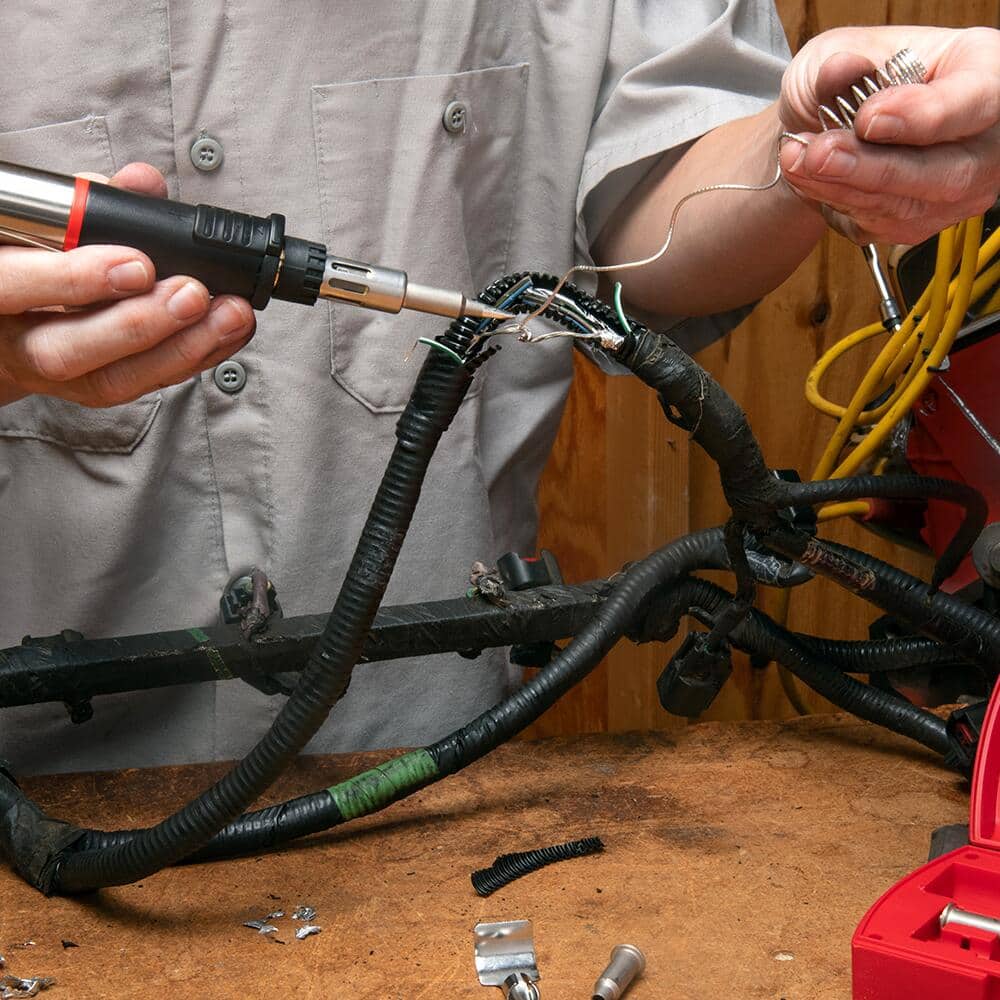 A man uses a soldering iron and solder to connect wires in a wiring harness.