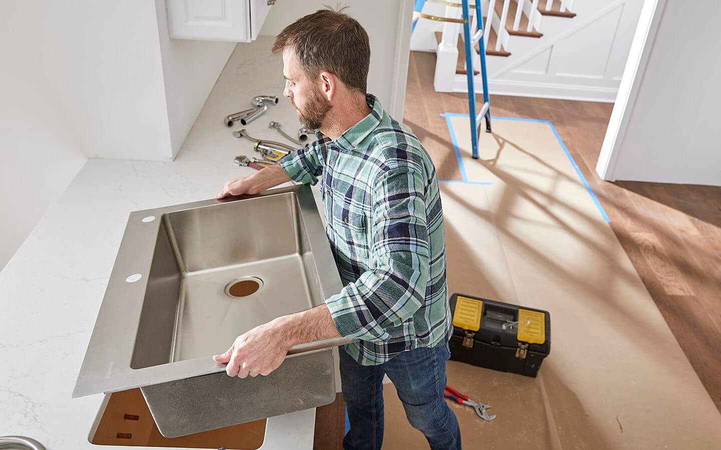 A new silver kitchen sink being installed in a white countertop. A new silver kitchen sink being installed in a white countertop.