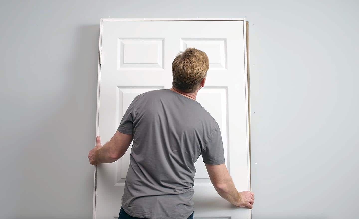 A man positioning a prehung door in a doorway.
