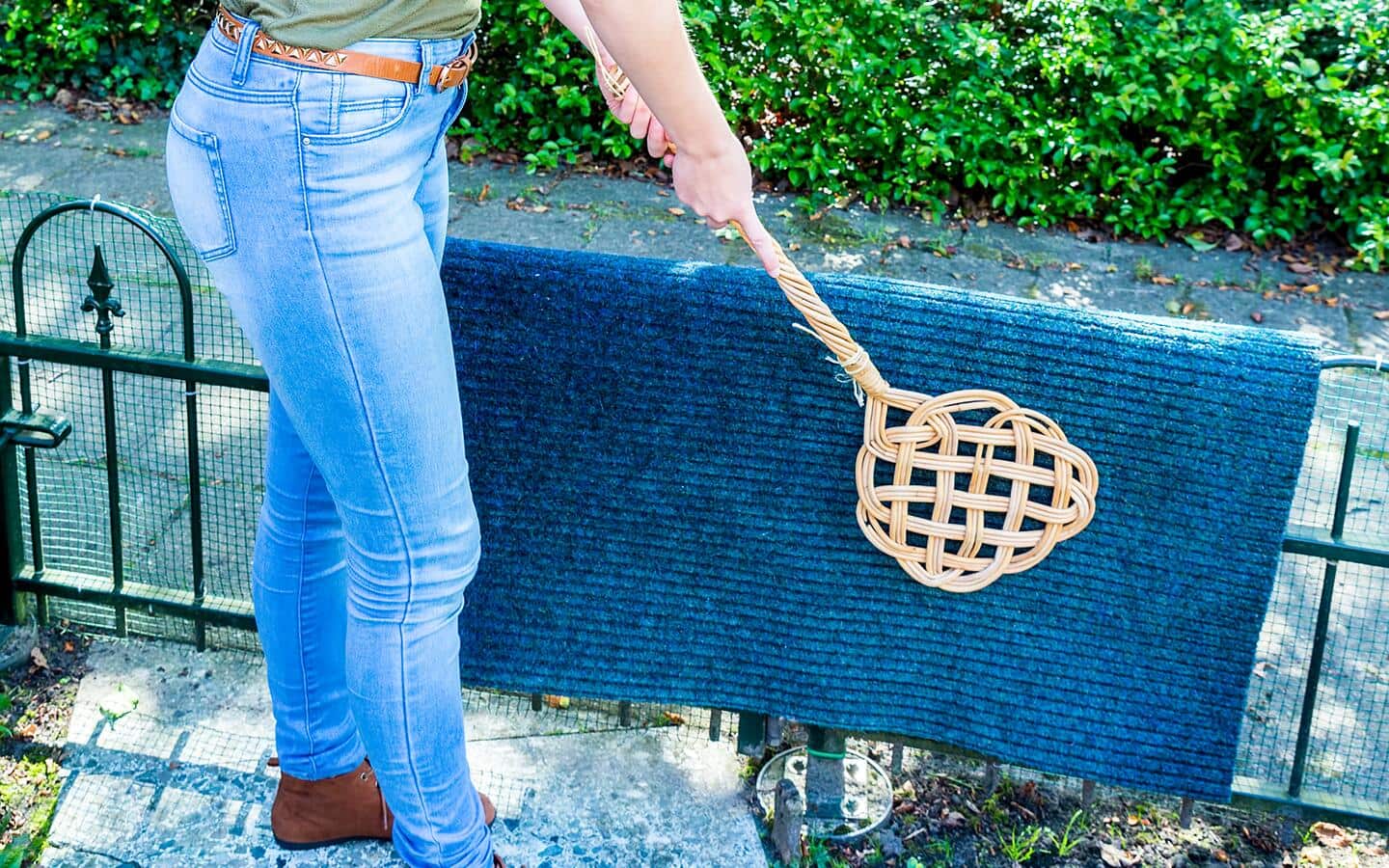 A person using a traditional rug beater to dust an area rug.