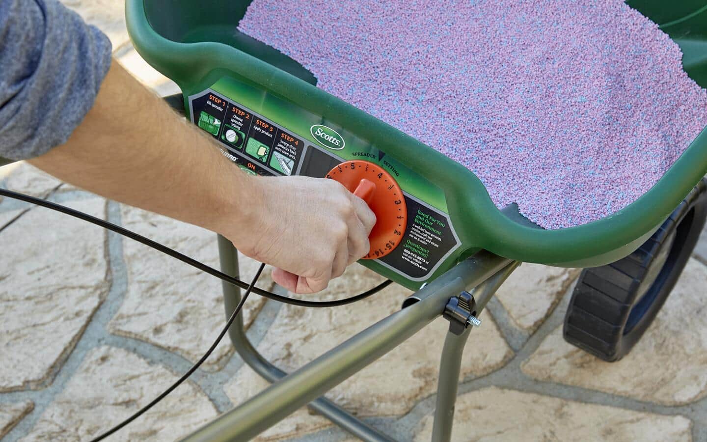 A person adjusts the dial on a spreader hopper. A person adjusts the dial on a spreader hopper.
