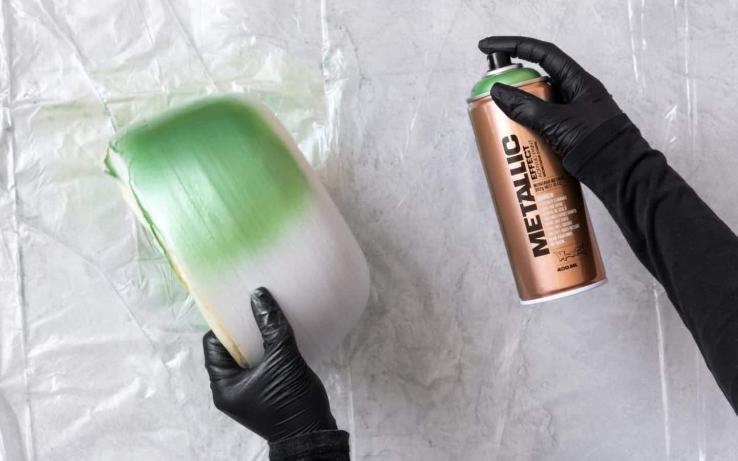 A person applying metallic spray paint to a clay bowl.