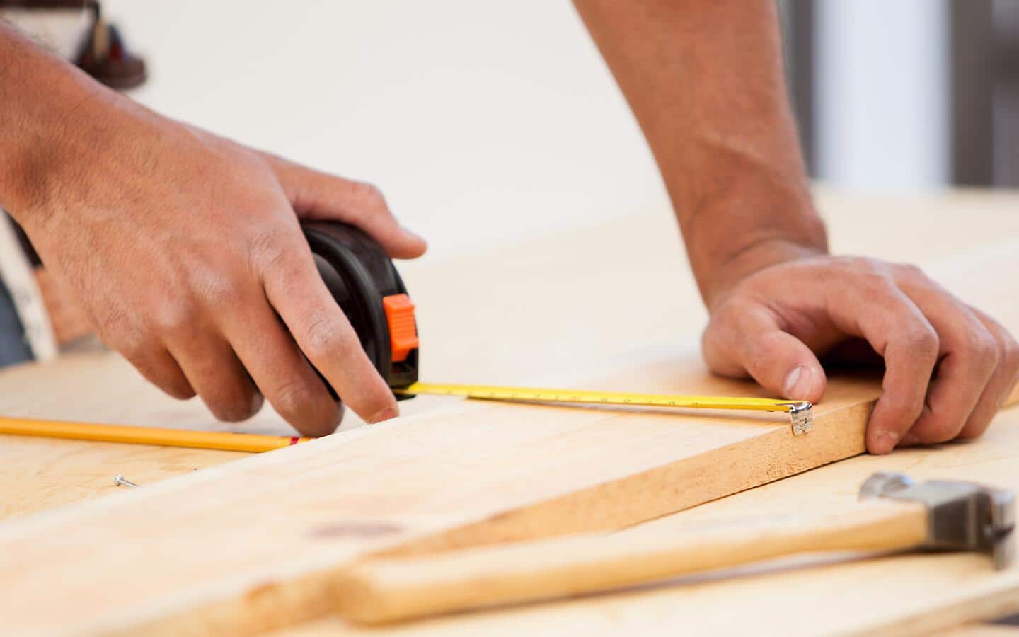 A person measures a board with a tape measure. A person measures a board with a tape measure.