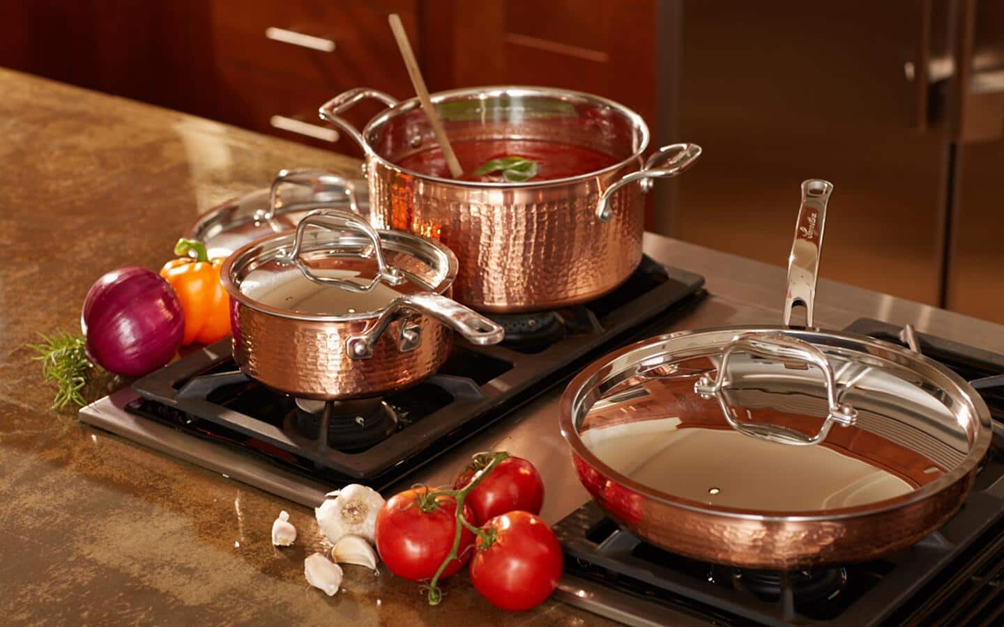 A copper cookware set of pots and pans sitting on cast iron stove top.