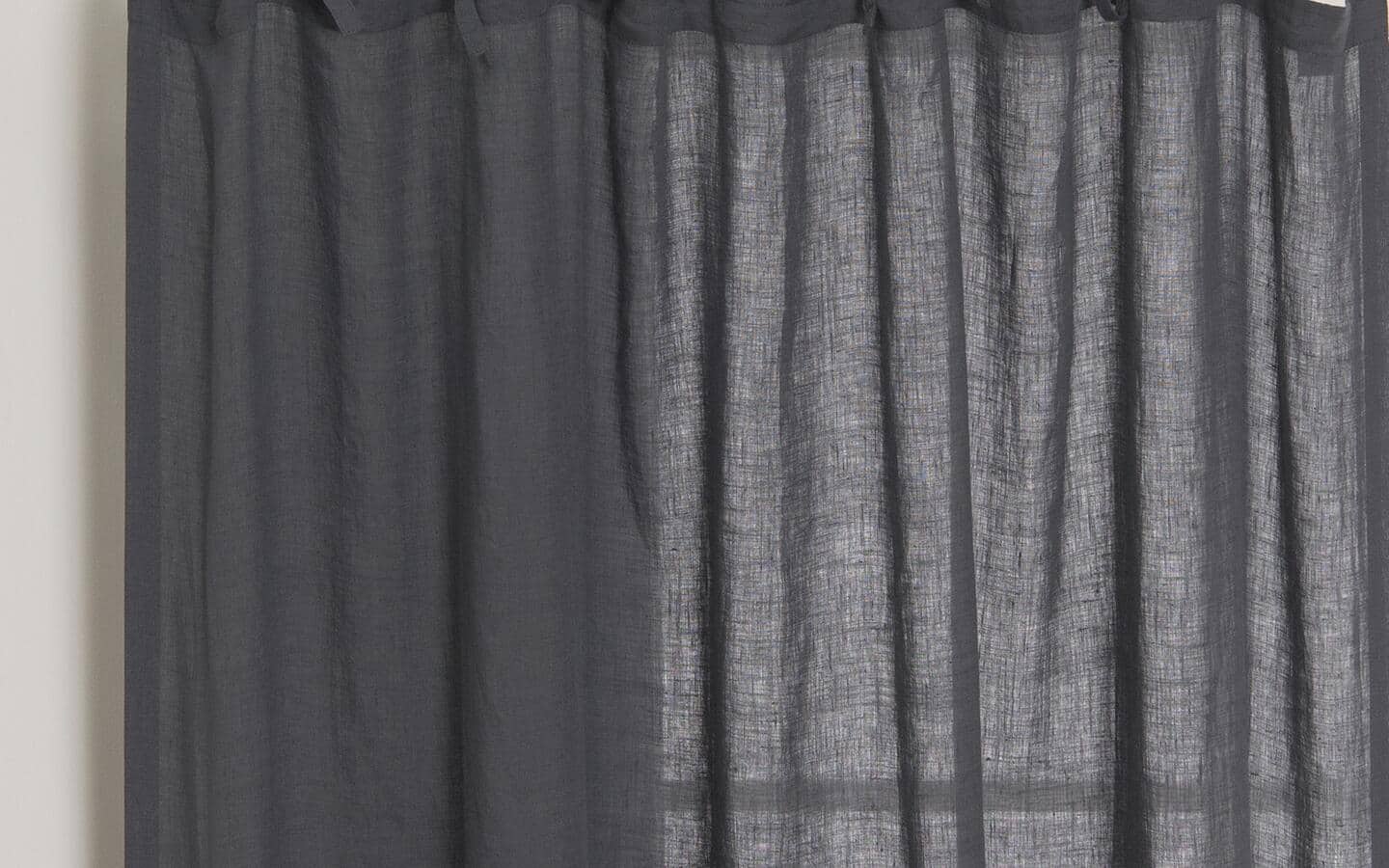 A dark-grey curtain with some light filtering in. A dark-grey curtain with some light filtering in.