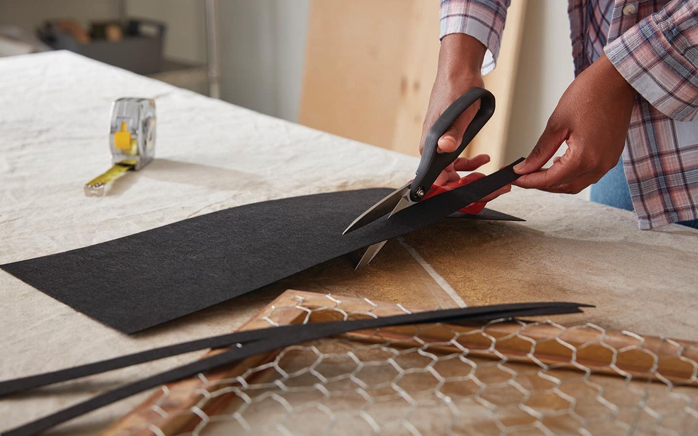 A person uses scissors to cut backing for a frame. A person uses scissors to cut backing for a frame.