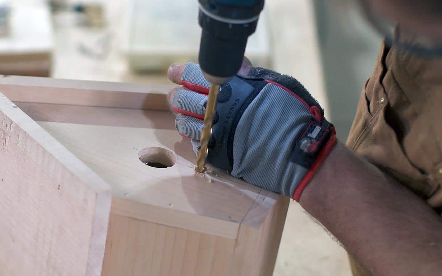 A person in gloves drills a hole for a birdhouse perch.
