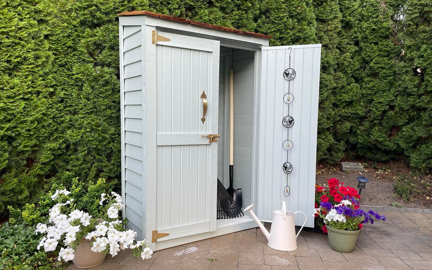 A light blue garden shed surrounded by colorful blooming planters and a water can.